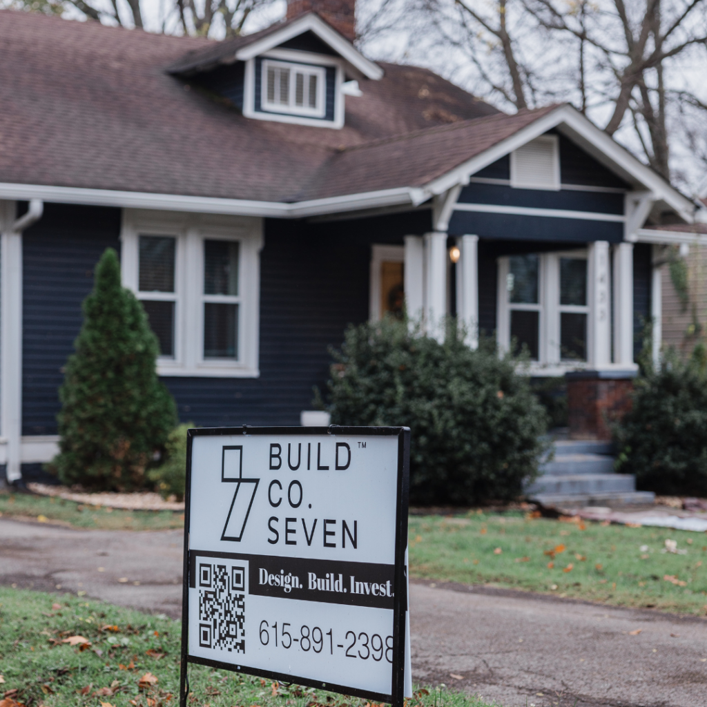 Renovated Craftsman-style home with dark blue siding and a BuildCo7 sign in the yard.