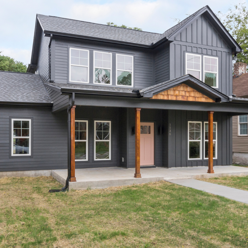 Modern farmhouse-style custom home with dark gray siding, wood accents, and a pink front door.