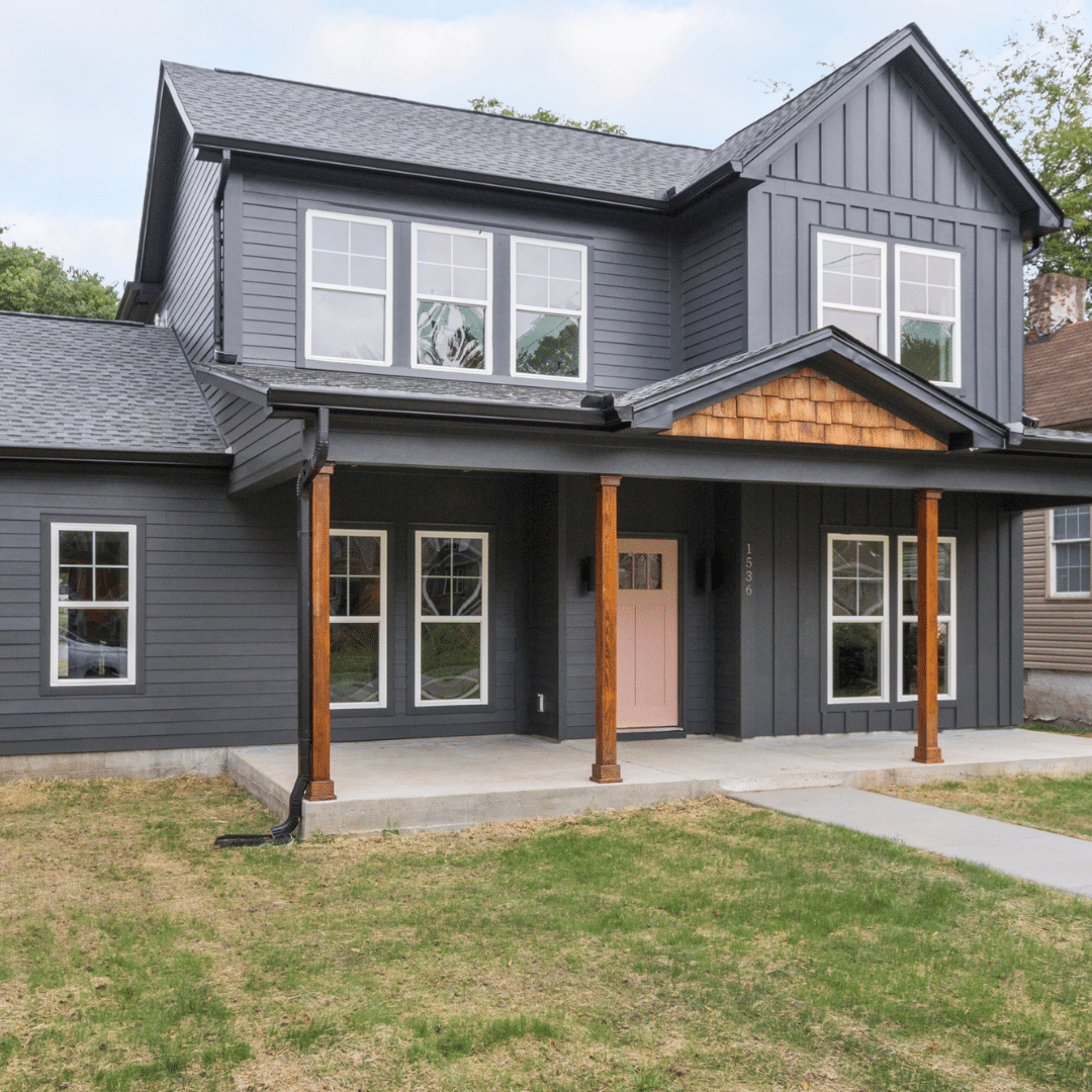 Modern farmhouse-style custom home with dark siding, wood accents, and a pink front door.