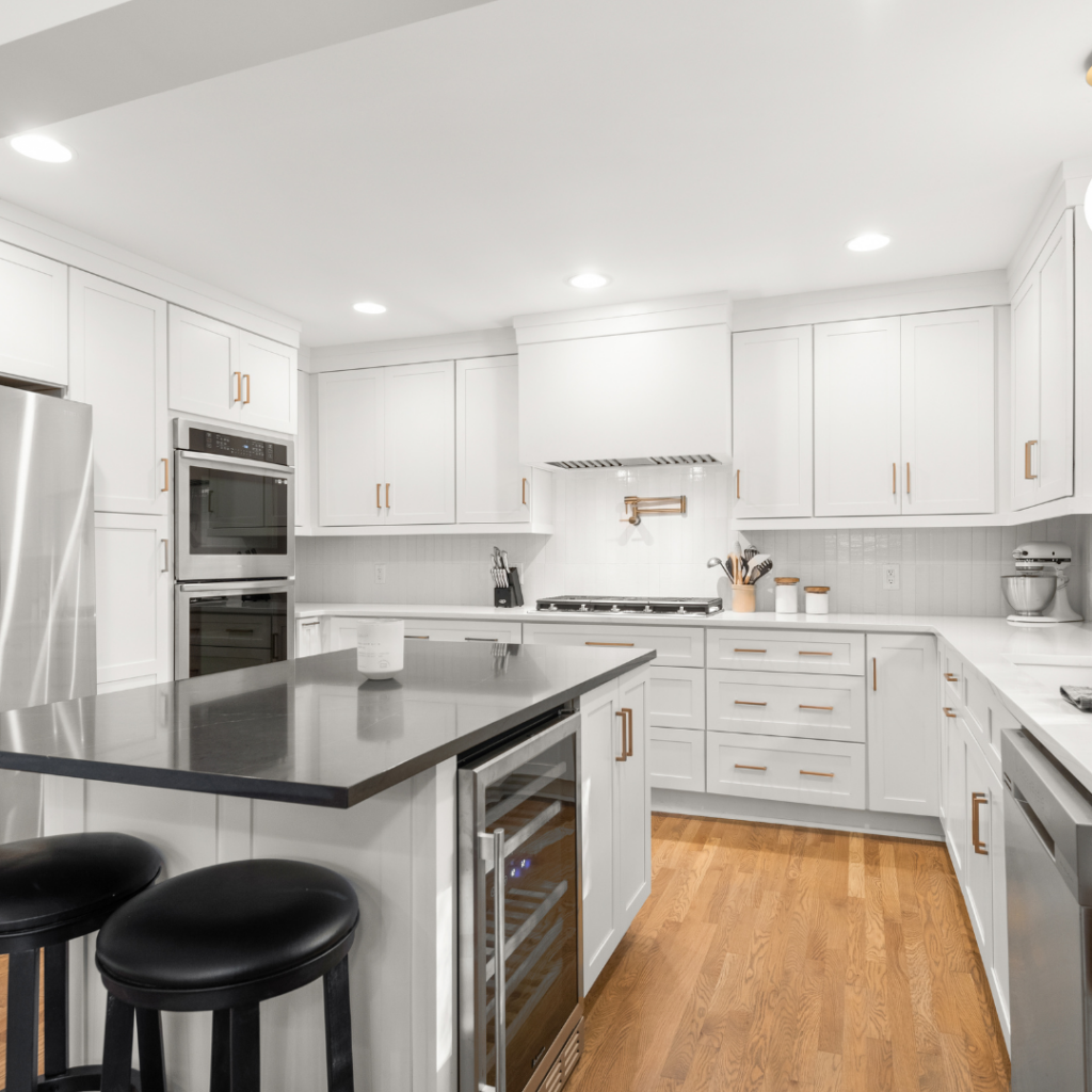 Elegant white kitchen with a black island, gold hardware, and built-in wine fridge.