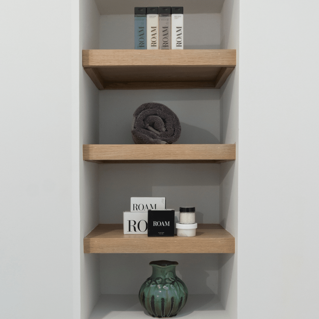 Modern built-in shelving with natural wood finish, neatly arranged with luxury bath products and a decorative vase.
