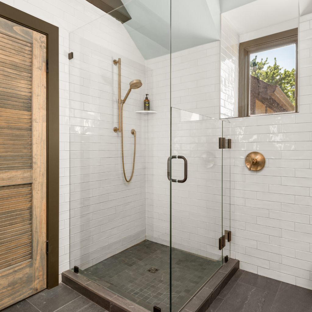 Modern glass shower with gold fixtures and subway tile walls.