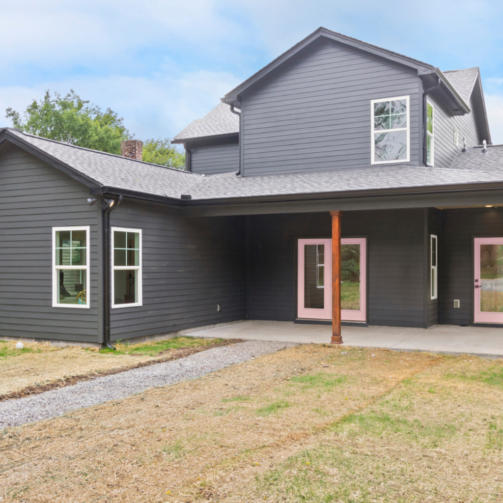 Modern farmhouse-style home with dark siding, pink doors, and a covered patio.