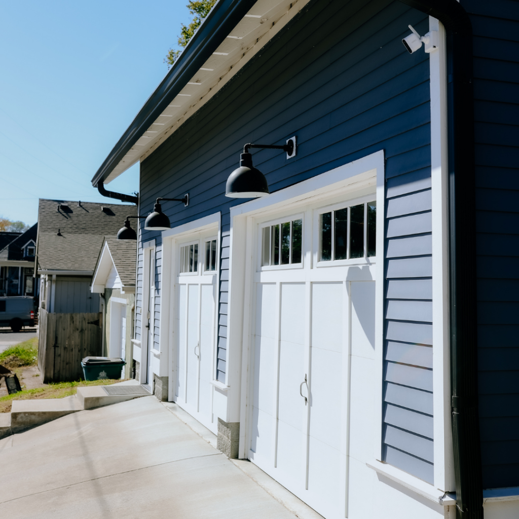 Modern blue DADU with white garage doors and black gooseneck lighting.